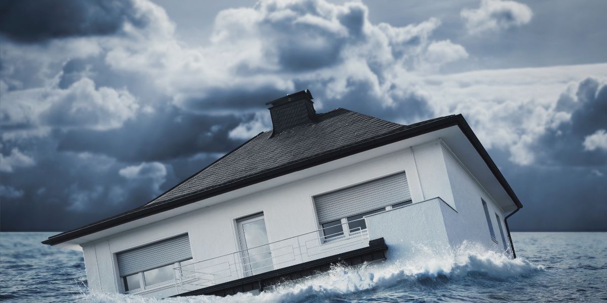 Modern house sinking into floodwaters under a stormy sky.