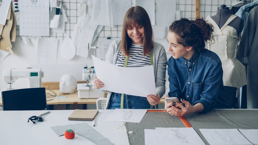 Two real estate professionals in a bright office looking closely at architectural blueprints spread across a wooden table, planning a home purchase.