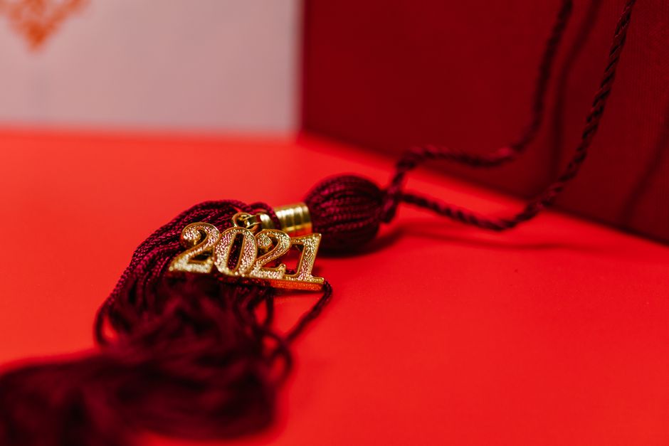 Miniature graduation cap sits on the roof of a white architectural model house against a bright, clean background, symboli...