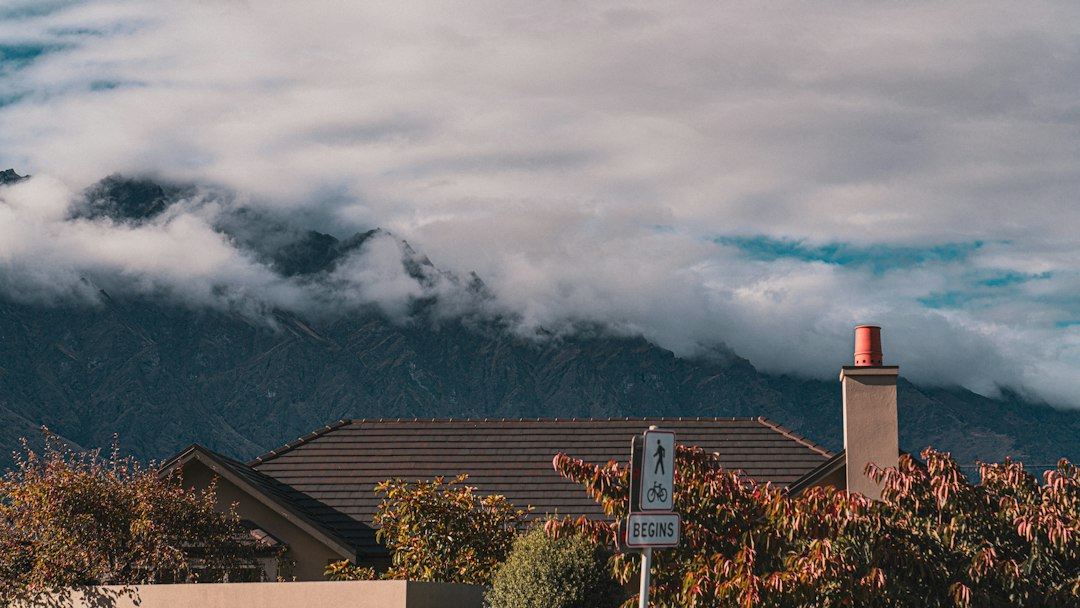 A professional real estate agent stands with a client in front of a house, pointing up to discuss the quality and condition of the roof.