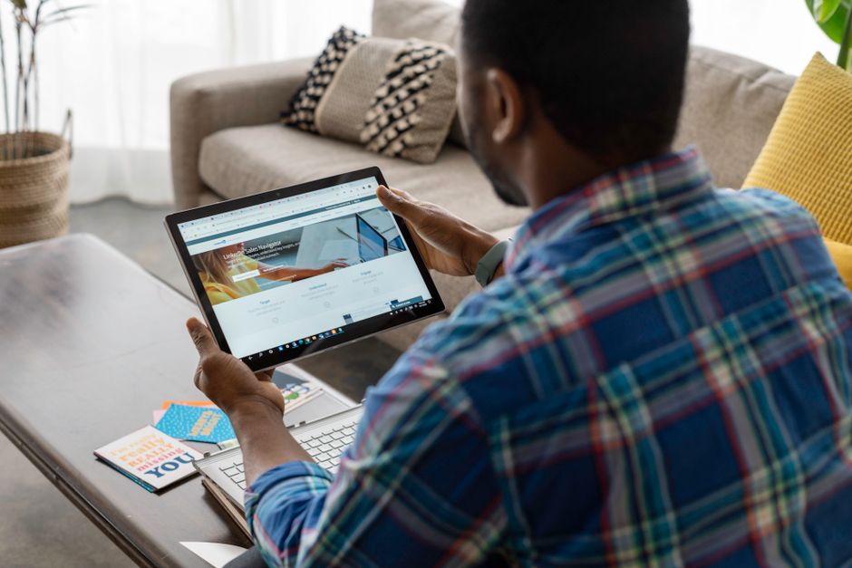 A real estate professional in a blazer shows a couple information on a tablet while sitting on a sofa in a bright, modern living room, representing a client consultation.